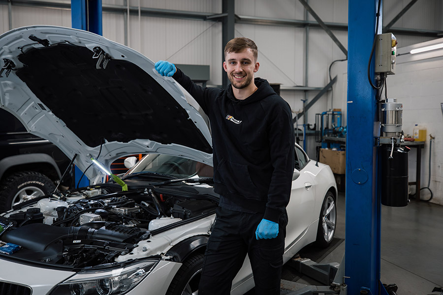 A motor vehicle apprentice standing taking a hero shot in front of a car with the bonnet open