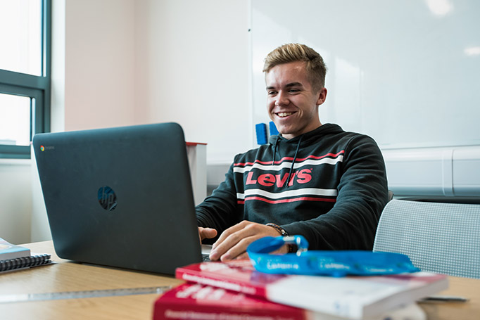 A student sat down on his laptop, smiling facing camera