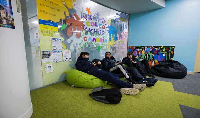 Three students sitting down on bean bags, in front of an equality wall display