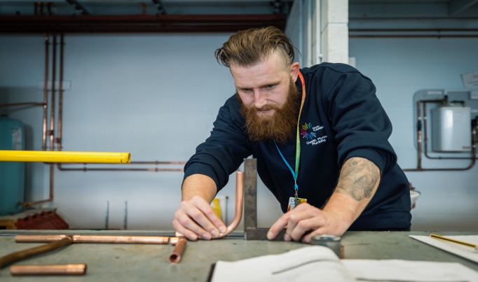 An adult learner measuring copper pipe