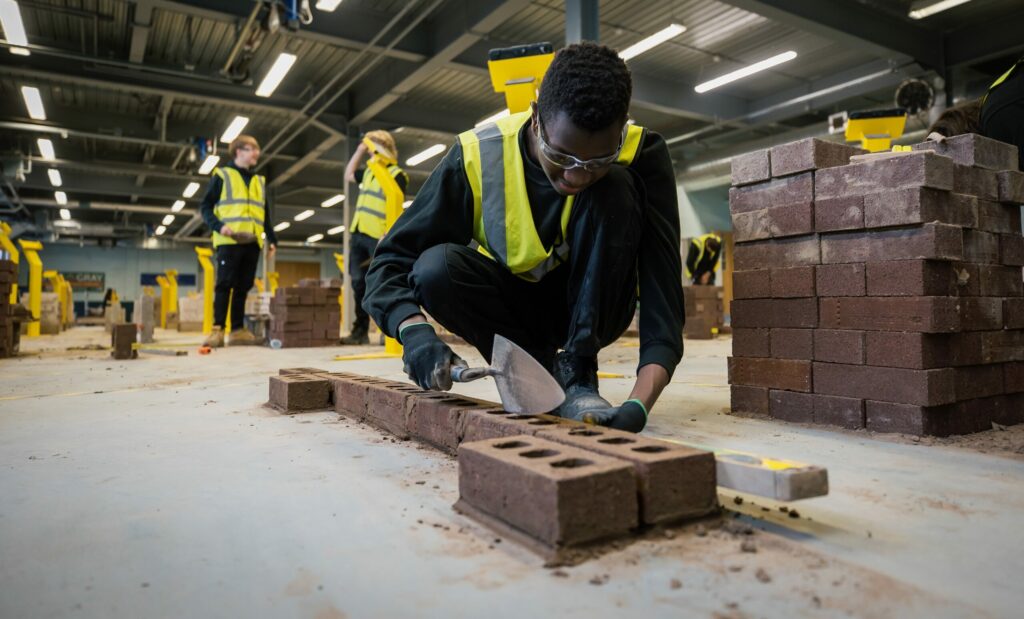 A brickwork student practicing laying bricks with two students behind