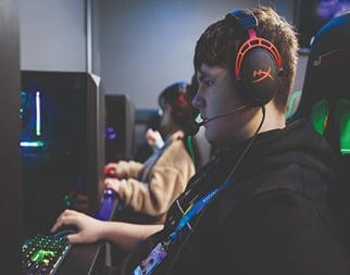 A side shot of three Esports students playing on gaming PC's with colourful equipment surrounding them