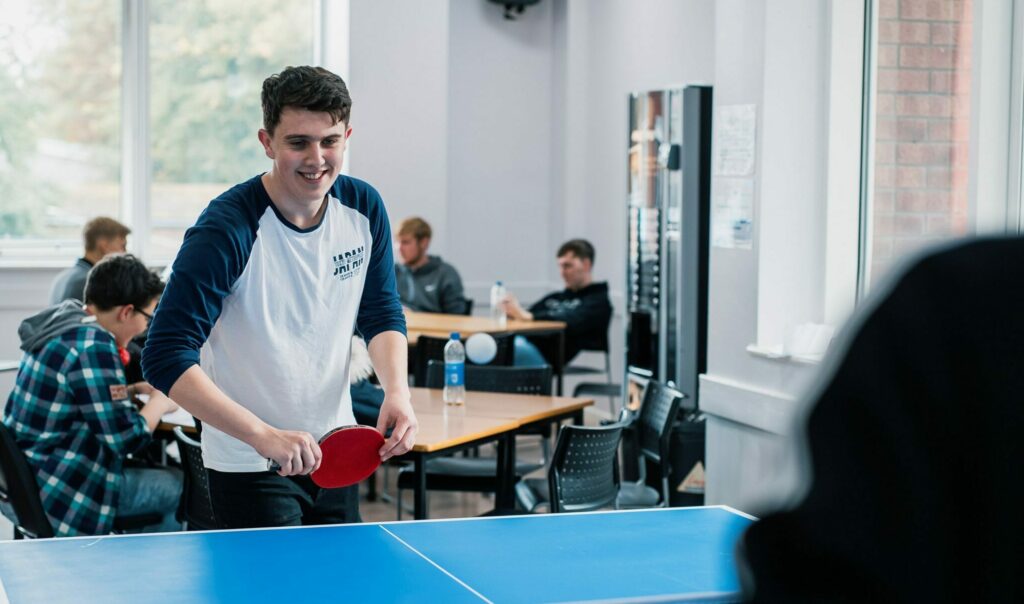 A student in one of the common areas playing table tennis.