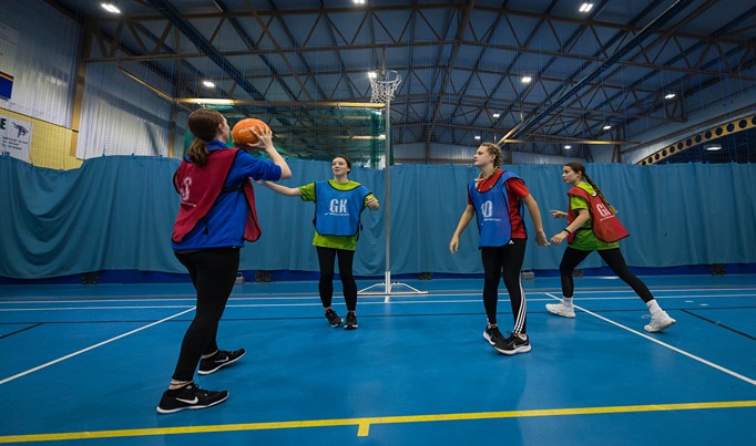 A group of four sports students playing netball in red and blue bibs