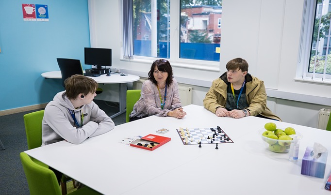 A member of staff sitting at a table having a conversation with two students who are sitting either side of her