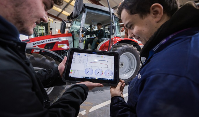 Two agriculture engineering students looking at a tablet with another student in the background sat in a tractor