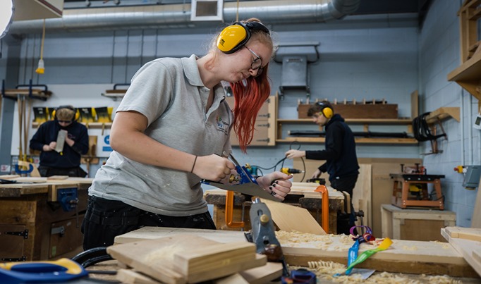 A carpentry and joinery learner using tools in a workshop to shave wood