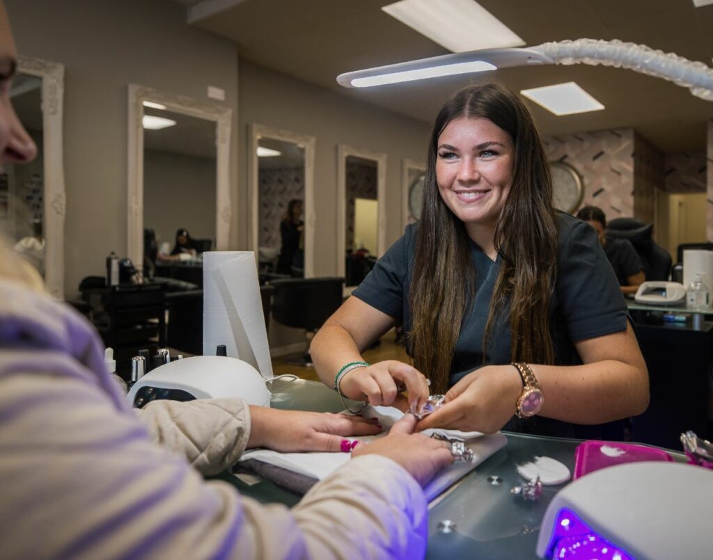 A beauty apprentice working at house of beauty smiling whilst doing the nails on a customer