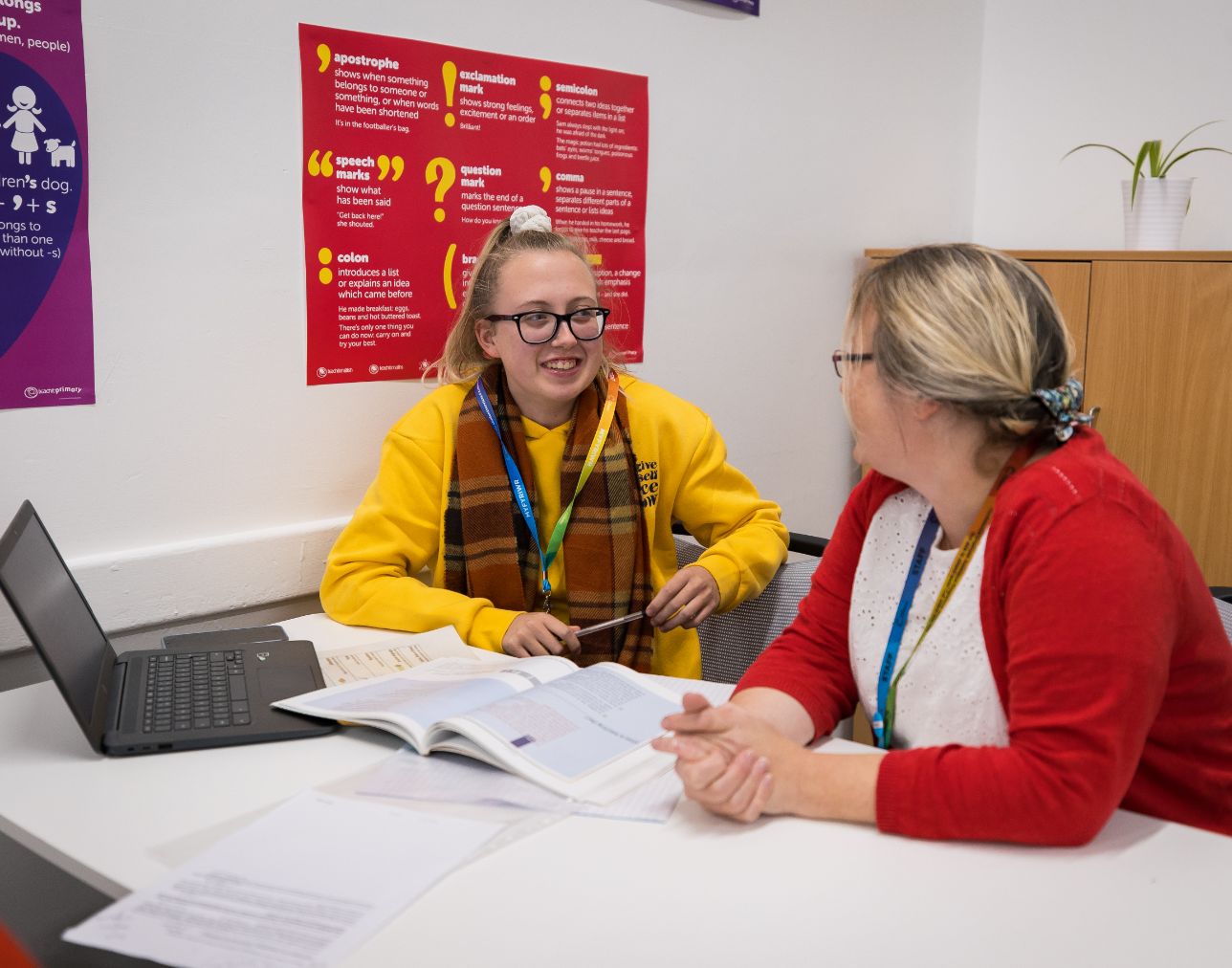 an English learner in a yellow jumper sat down at a desk next to a tutor talking