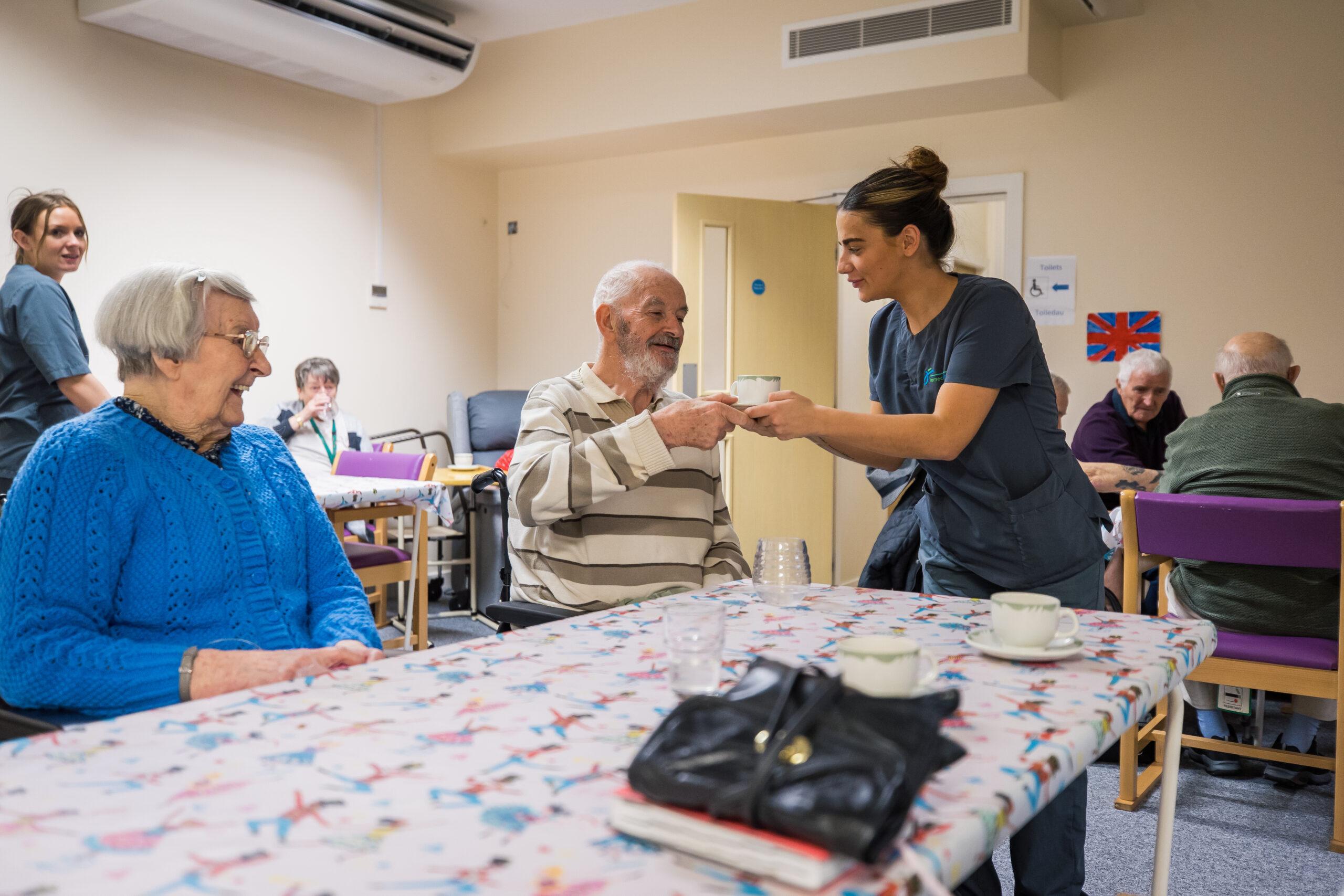 Health & Social Care Apprentice handing a drink to an elderly man