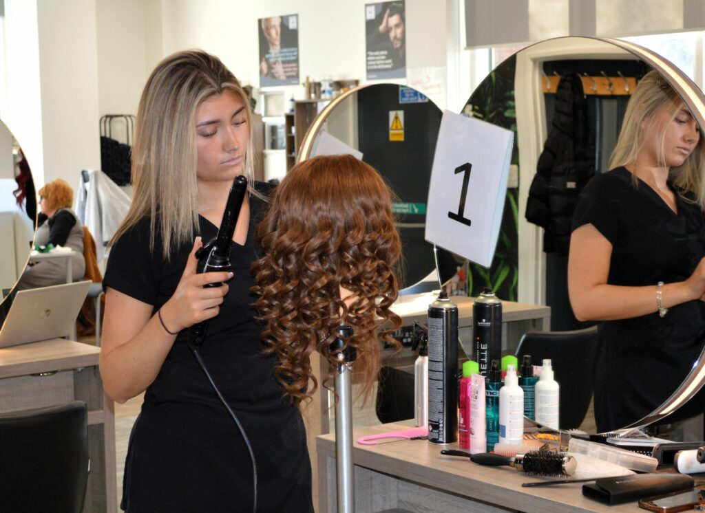 A skills competitor curling the hair on a wig for the news post 'LEARNERS and apprentices representing Coleg Cambria and its industry partners shone at this year’s Skills Competition Wales'