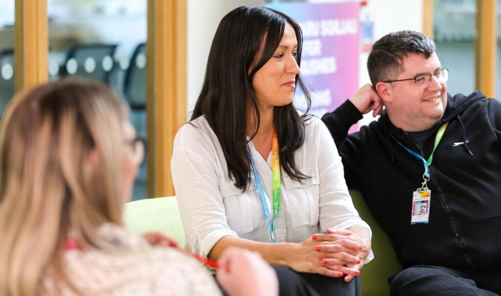 A close up shot of three adult learners sat on sofas mid conversation