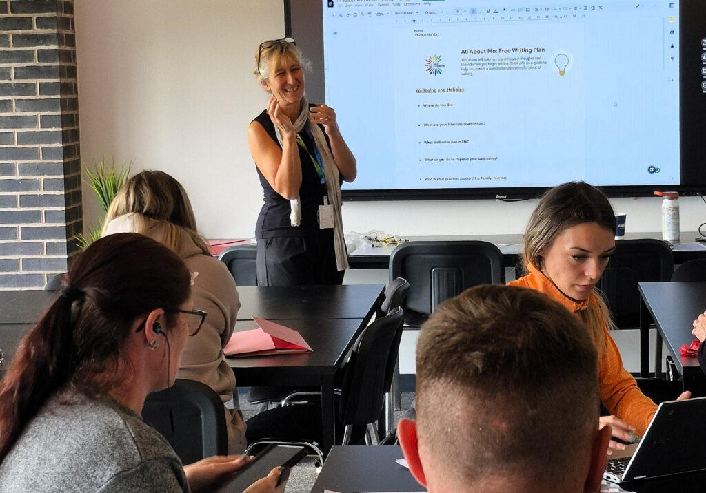 a tutor stood at the front of a class in front of a large screen