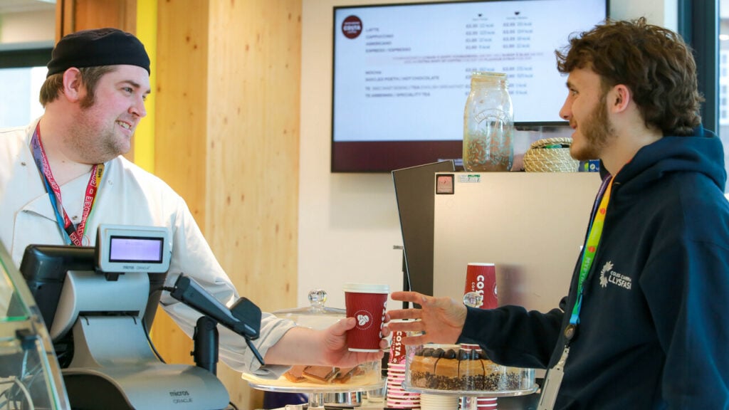 a cafe worker handing a coffee to a student