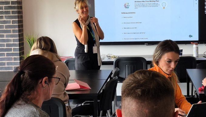 a tutor stood at the front of a class in front of a large screen