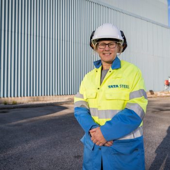 Photo of April Wilkinson wearing TATA Steel safety wear stading outside of on of their buildings