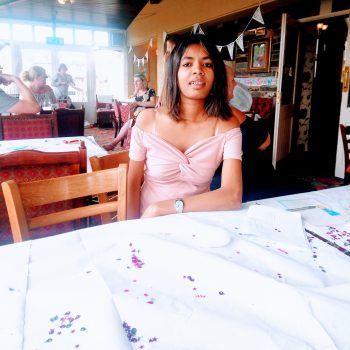 A learner in a pink top smiling and sat at a table.