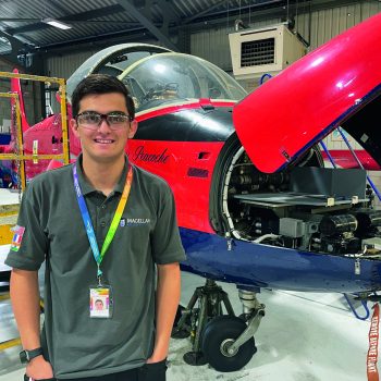 Photo of Aeronautical Apprentice Joe Williams stading next to a plane in the workshop