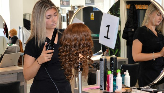 A skills competitor curling the hair on a wig for the news post 'LEARNERS and apprentices representing Coleg Cambria and its industry partners shone at this year’s Skills Competition Wales'